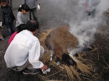 わらで覆った上にさらに粘土をかぶせ、裾から点火。最初は徐々に温度を上げます。